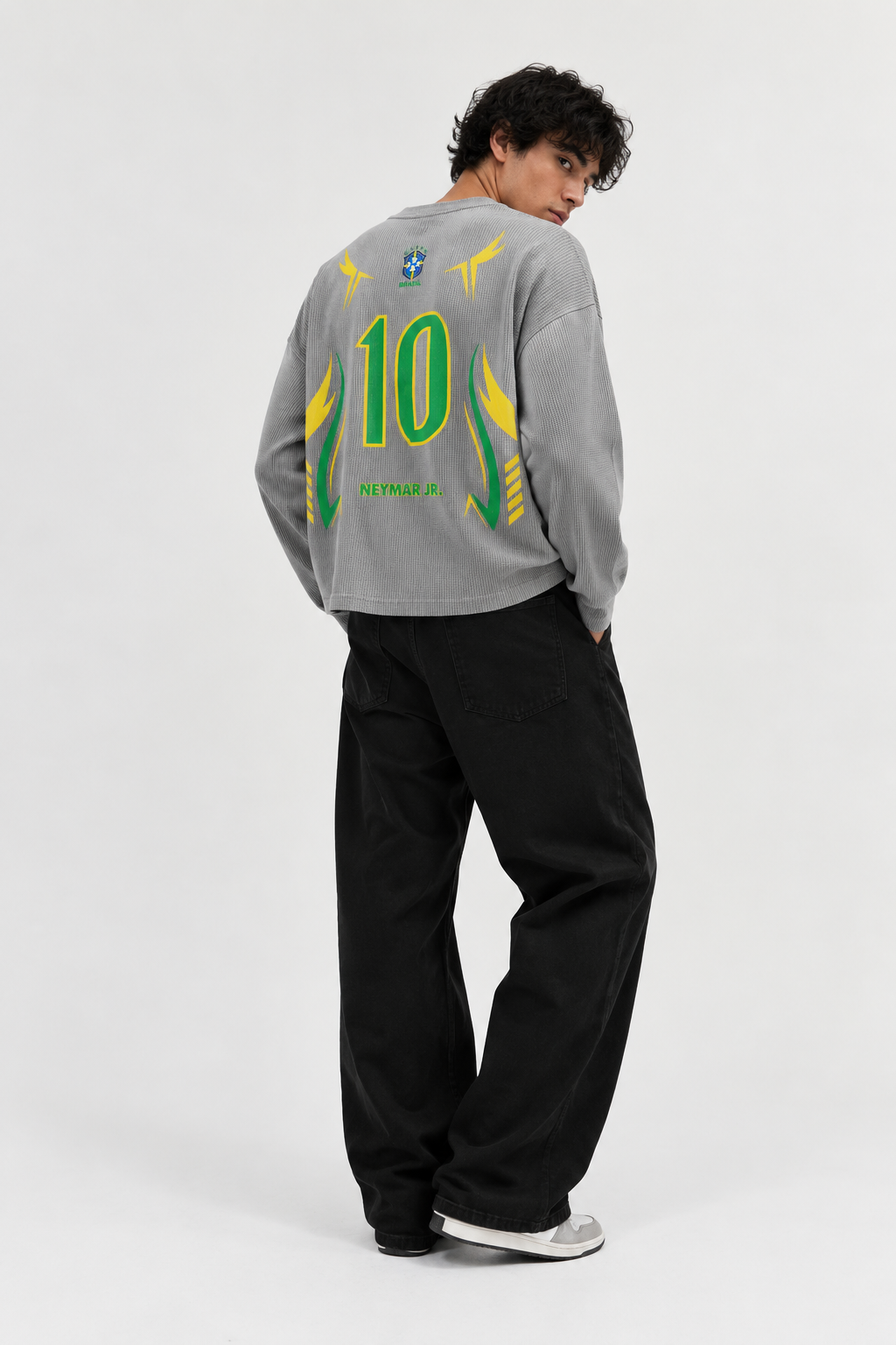 A model wearing a RFLXNS long-sleeve waffle Tshirt with a green and yellow number 10 back print, paired with black pants, on a light gray studio background.